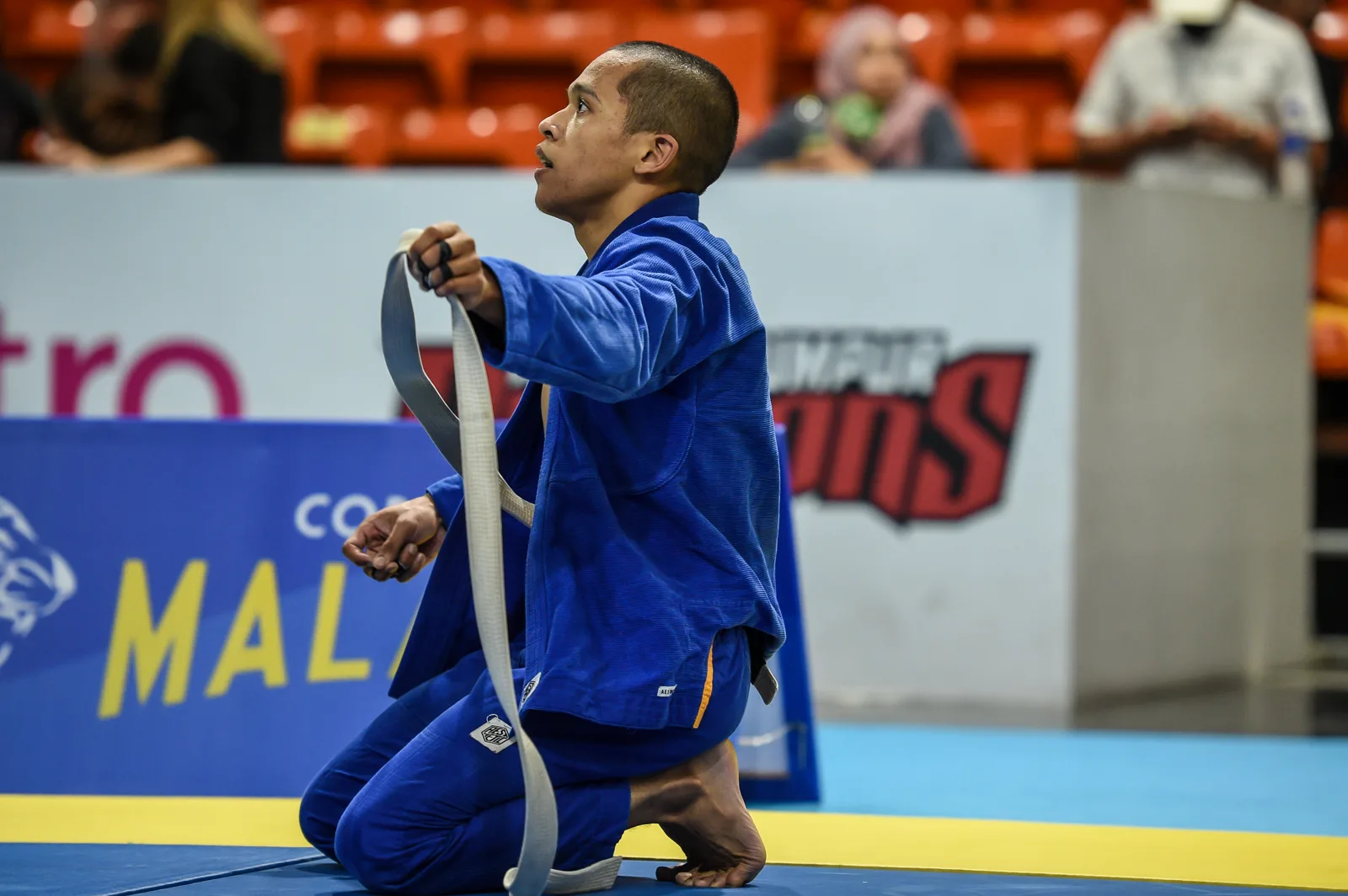 Coach Aiman kneeling on the competition mat, tying his belt before a match